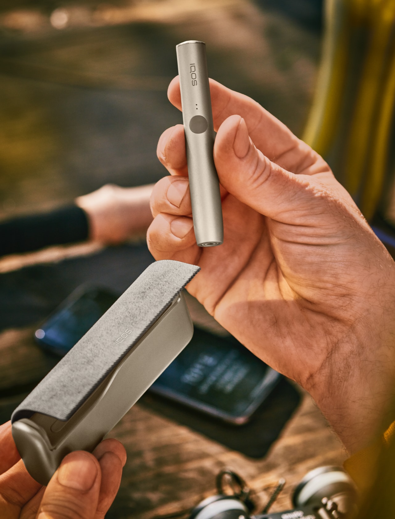 An IQOS IUMA device held in one hand and the charger in another.